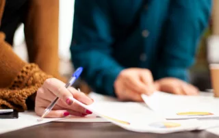 Two people reviewing documents with colorful charts and pen, collaborating on mortgage forbearance vs. loan modification concepts