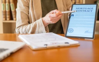 Person reviewing a digital mortgage contract on a tablet with documents and a pen, representing mortgage modification options that can lower payments or help homeowners catch up on missed payments.